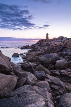 a lighthouse on a rocky shore at sunset